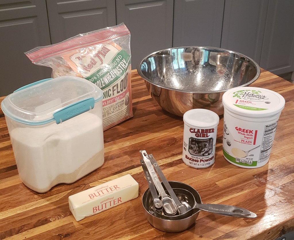 Butter, sugar, flour, big silver bowl, baking powder, Greek yogurt and measuring spoons and cups.