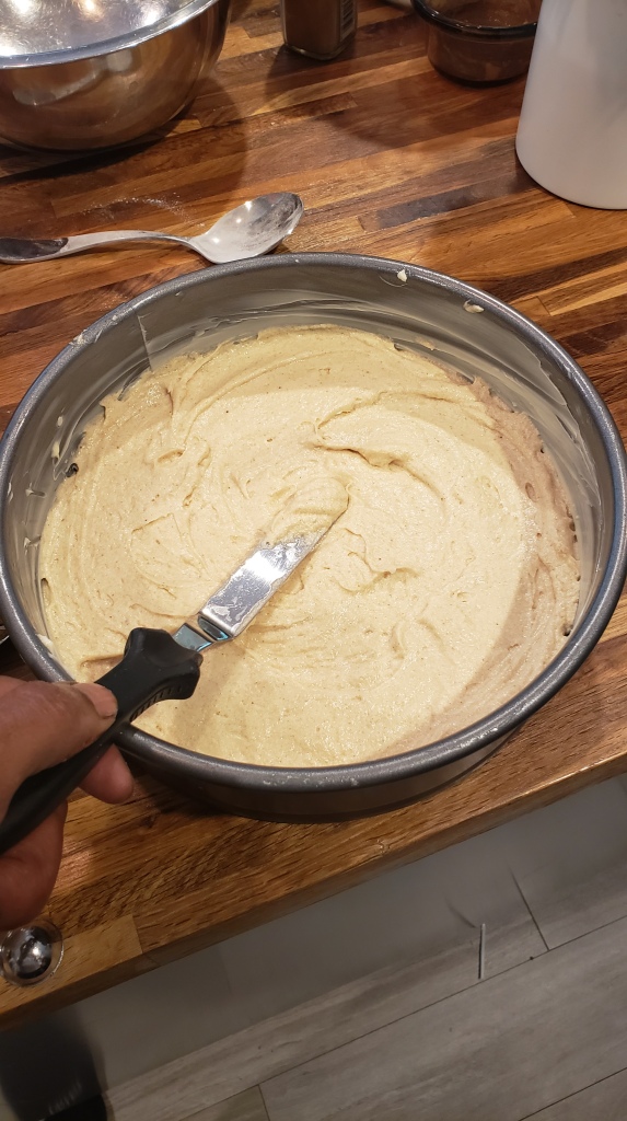Raw cake batter is spread into a greased springform pan.